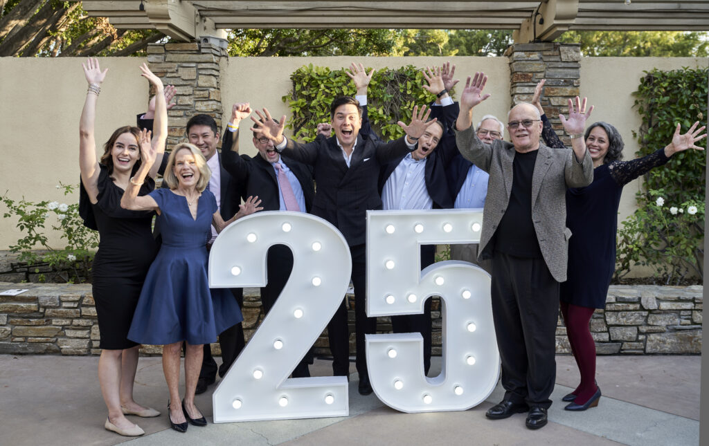 IEA Board members happily standing around marquee 25 lights with their hands raised in celebration